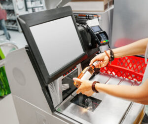 A person holds out a bottle of wine for the price scanner at a grocery store self-checkout station