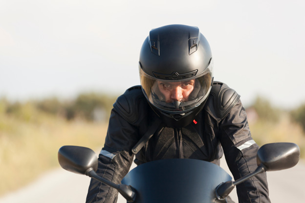 A close-up shot of a motorcyclist wearing a black helmet and protective gear, focused and looking straight ahead