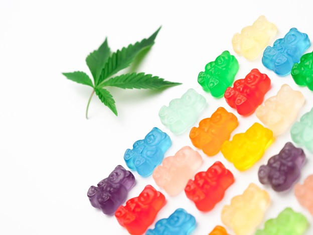 A marijuana leaf is pictured alongside rows of colorful gummy bear edibles on a white background